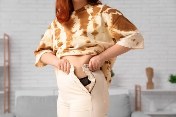 Image of woman trying to do her trousers up after pregnancy weight gain Coatbridge